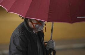 ep una mujer con una peculiar mascarilla se resguarda de la lluvia bajo su paraguas durante el dia