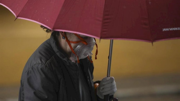 ep una mujer con una peculiar mascarilla se resguarda de la lluvia bajo su paraguas durante el dia