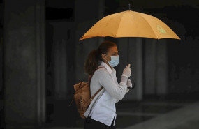 ep una mujer protegida con mascarilla y guantes se resguarda de la lluvia bajo su paraguas en la 20200512081202