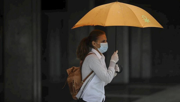 ep una mujer protegida con mascarilla y guantes se resguarda de la lluvia bajo su paraguas en la 20200512081202