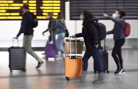 ep varias personas con maletas pasan junto a un panel de salidas con diferentes destinos en la
