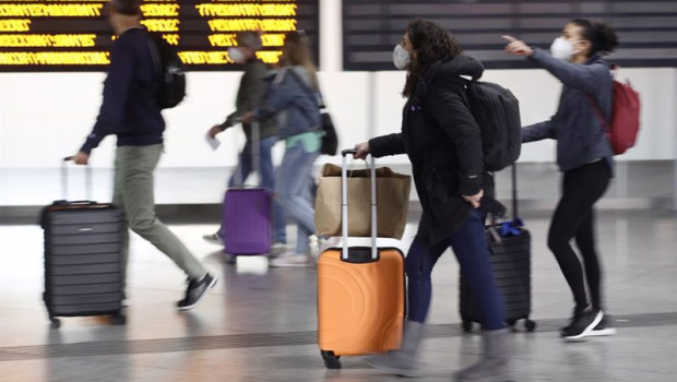ep varias personas con maletas pasan junto a un panel de salidas con diferentes destinos en la