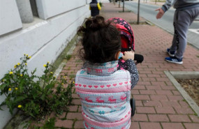 ep una nina pasea por la calle empujando un carrito con un bebe de juguete junto a su padre y su