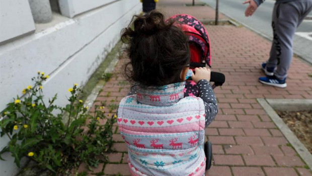ep una nina pasea por la calle empujando un carrito con un bebe de juguete junto a su padre y su