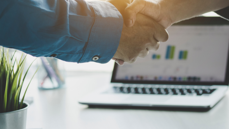 dos manos apretndose y un ordenador al fondo